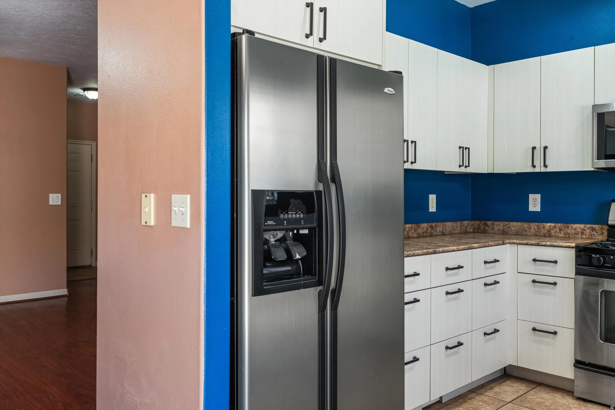 Kitchen featuring stainless steel side-by-side refrigerator, white cabinetry with black hardware, and speckled countertops