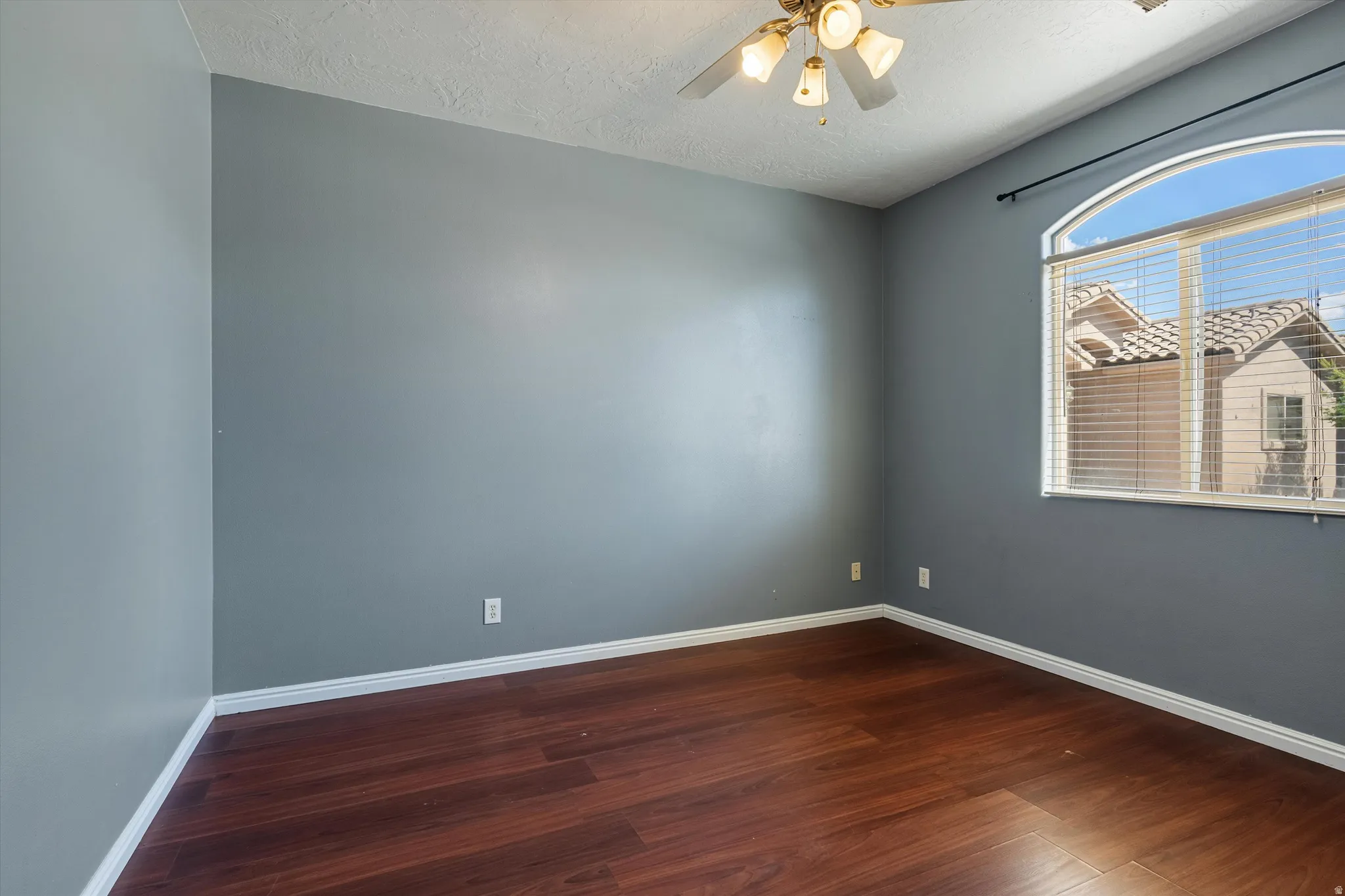 Room featuring wood-finish flooring, a ceiling fan with integrated lighting, and an arched window with blinds