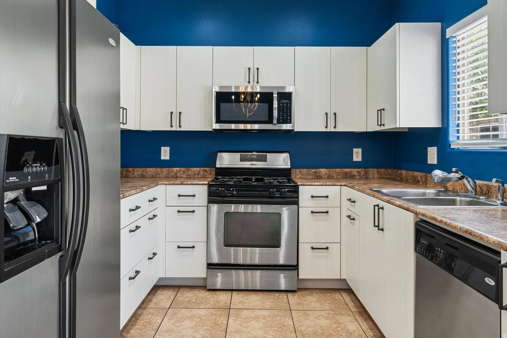 U-shaped kitchen featuring white cabinetry with dark pulls, stainless steel appliances, and a double basin sink