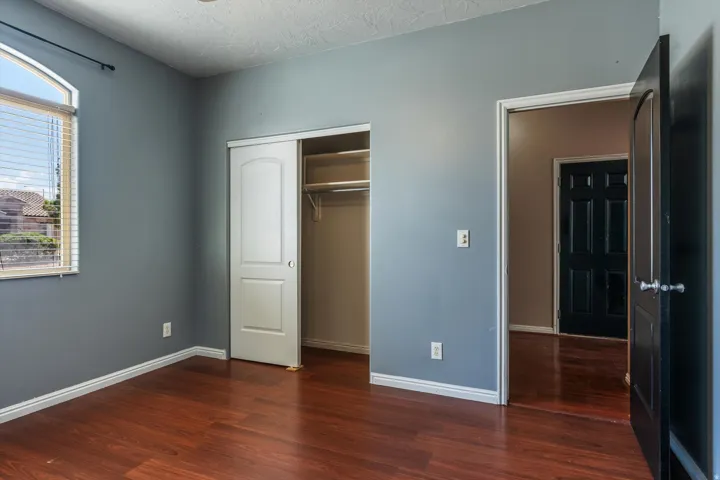 Room featuring wood-finish flooring, a sliding closet door with shelving and hanging rods, and an arched window with blinds