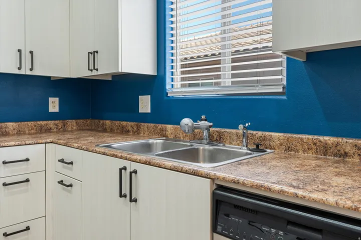 Kitchen featuring a stainless steel double-basin sink, light-toned cabinetry with dark hardware, and speckled countertops