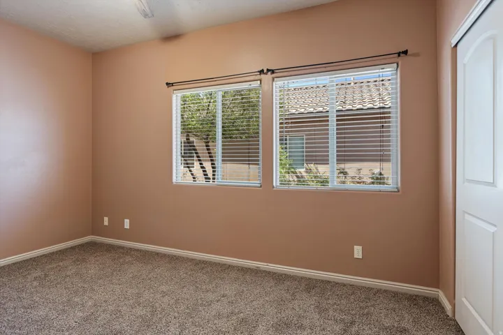 Carpeted interior room featuring two windows with horizontal blinds, a white paneled door, and a ceiling fan