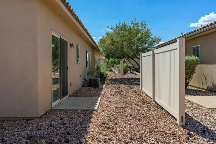 Side yard area featuring a concrete patio, sliding glass door, stucco exterior, and gravel landscaping