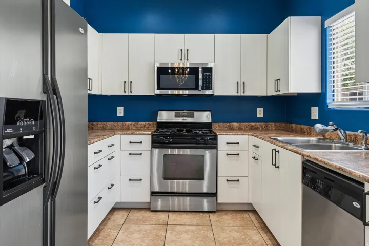U-shaped kitchen featuring white cabinetry with dark pulls, stainless steel appliances, and a double basin sink