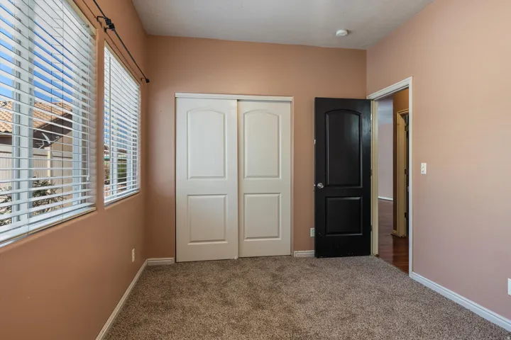 Room with two windows featuring horizontal blinds, textured carpeting, a double-panel closet with white doors, and a contrasting black interior door