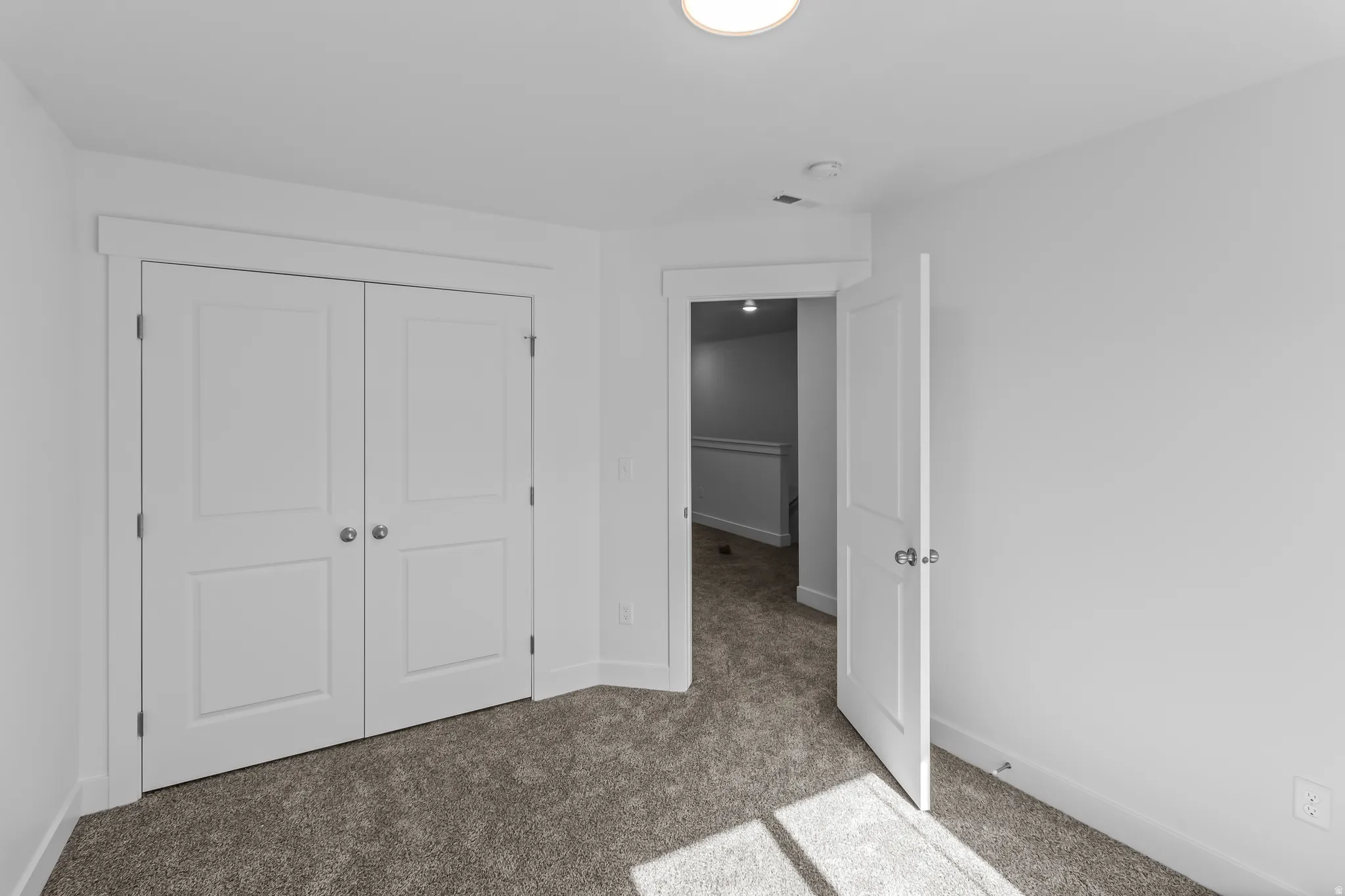 Bright room featuring neutral-toned carpet, white walls, and a prominent double-door closet with panel detailing