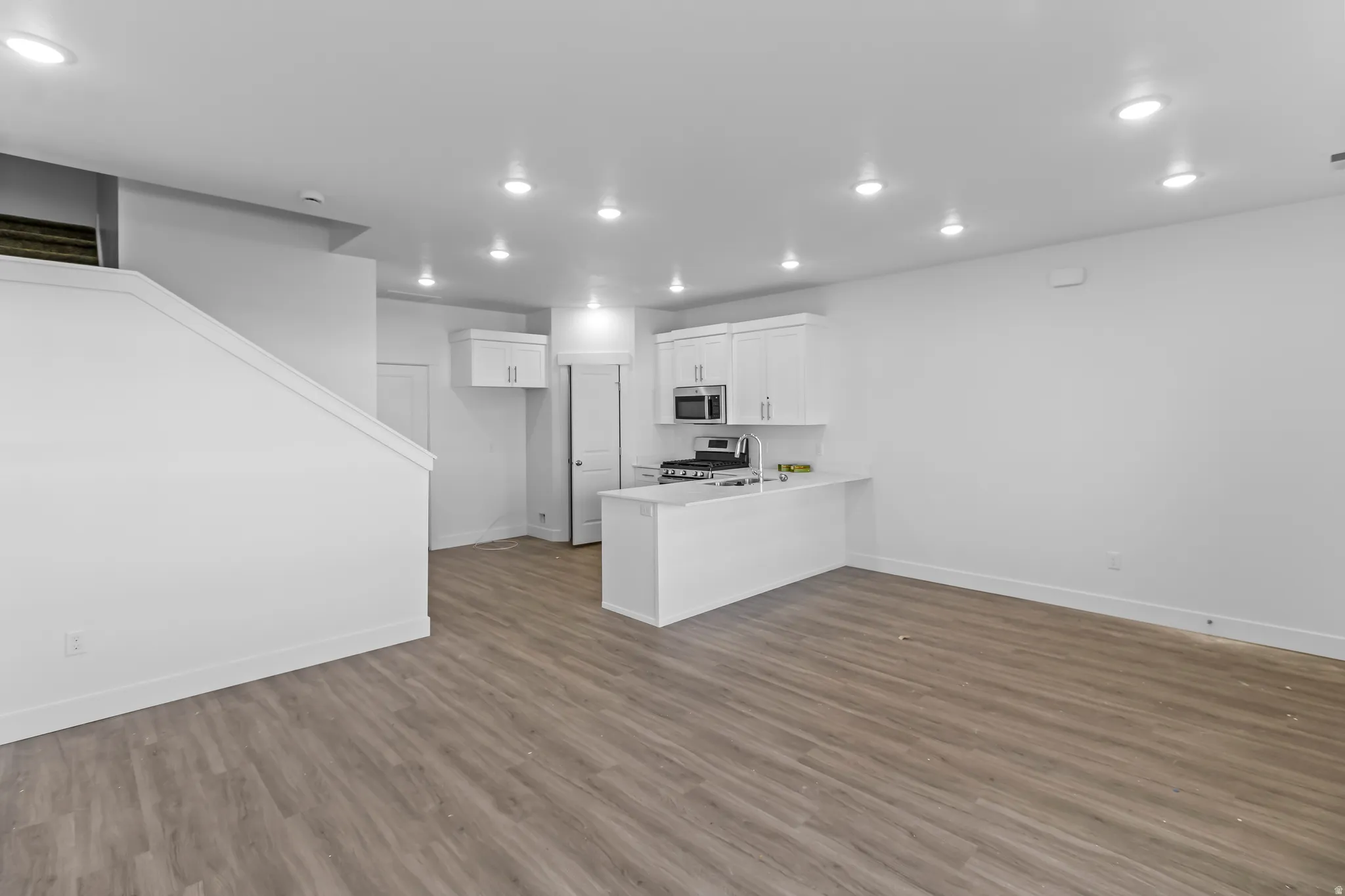 Open-concept living area featuring wood-finish flooring, recessed lighting, and a kitchen with white cabinetry, stainless steel appliances, and a peninsula with countertop seating