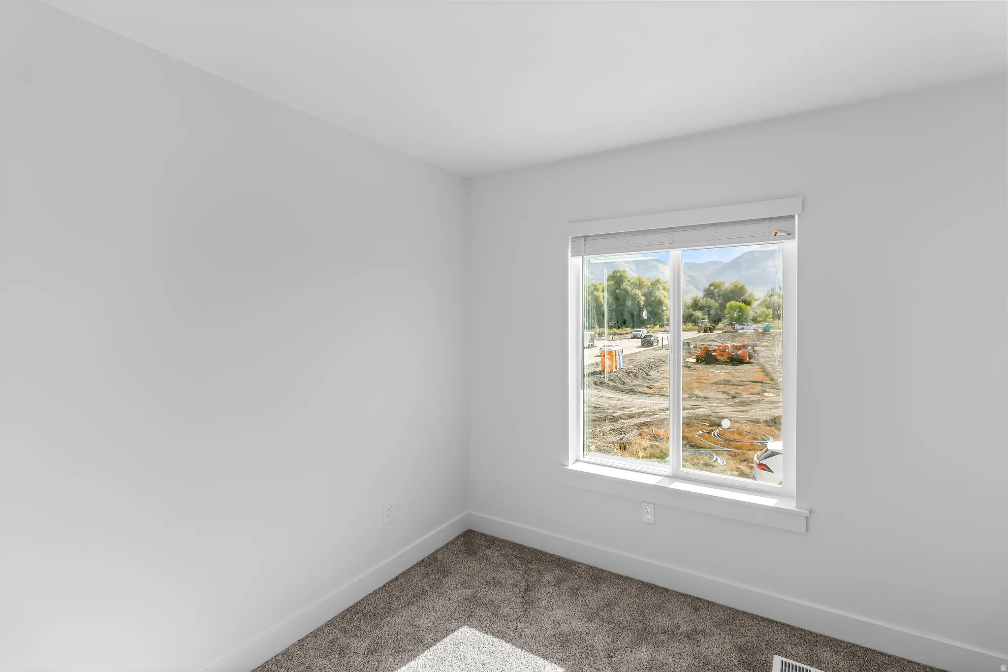 Bright room featuring a large window, neutral wall paint, white trim, and textured carpeting