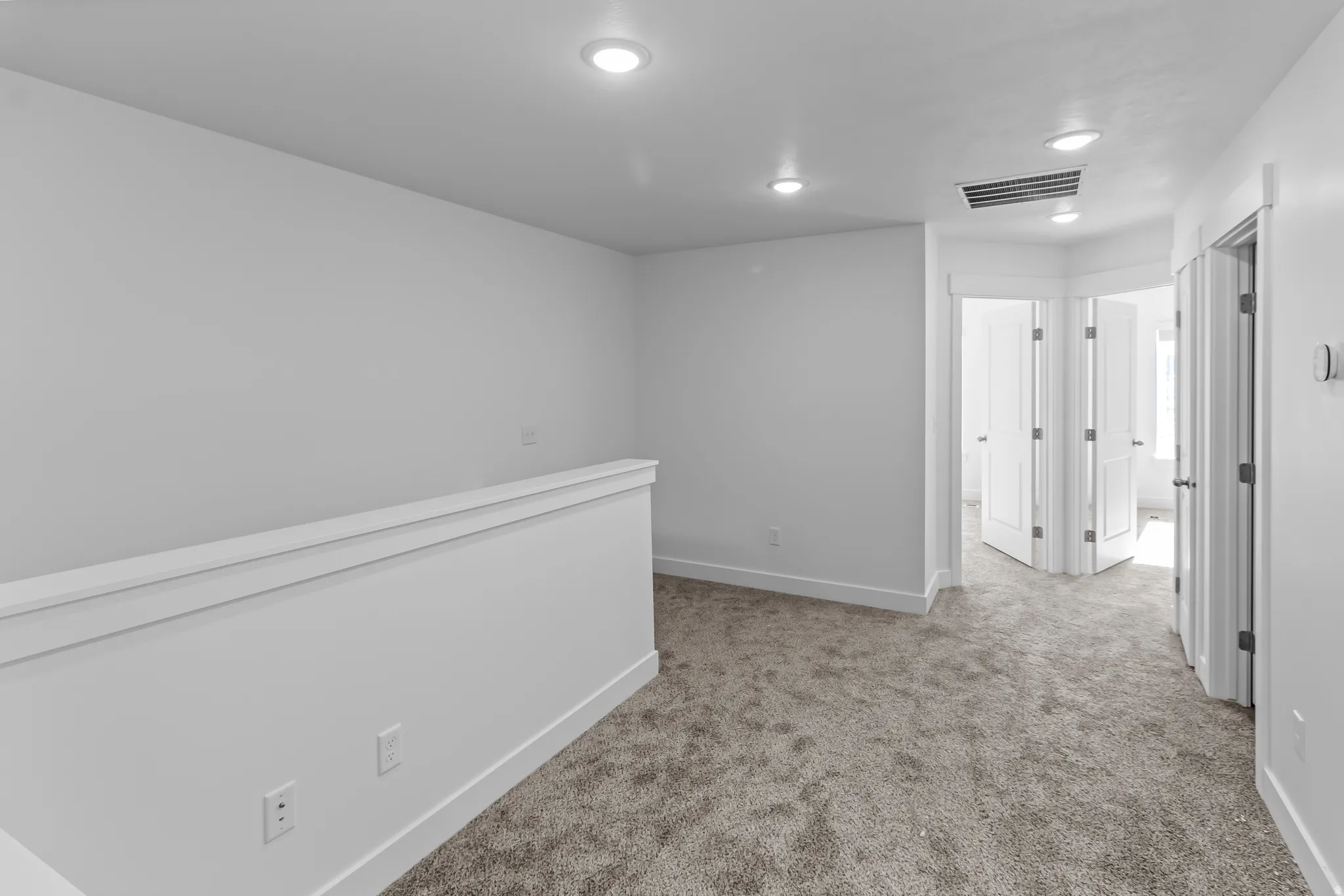 Upper-level landing featuring neutral carpeting, a white half-wall railing, and recessed lighting