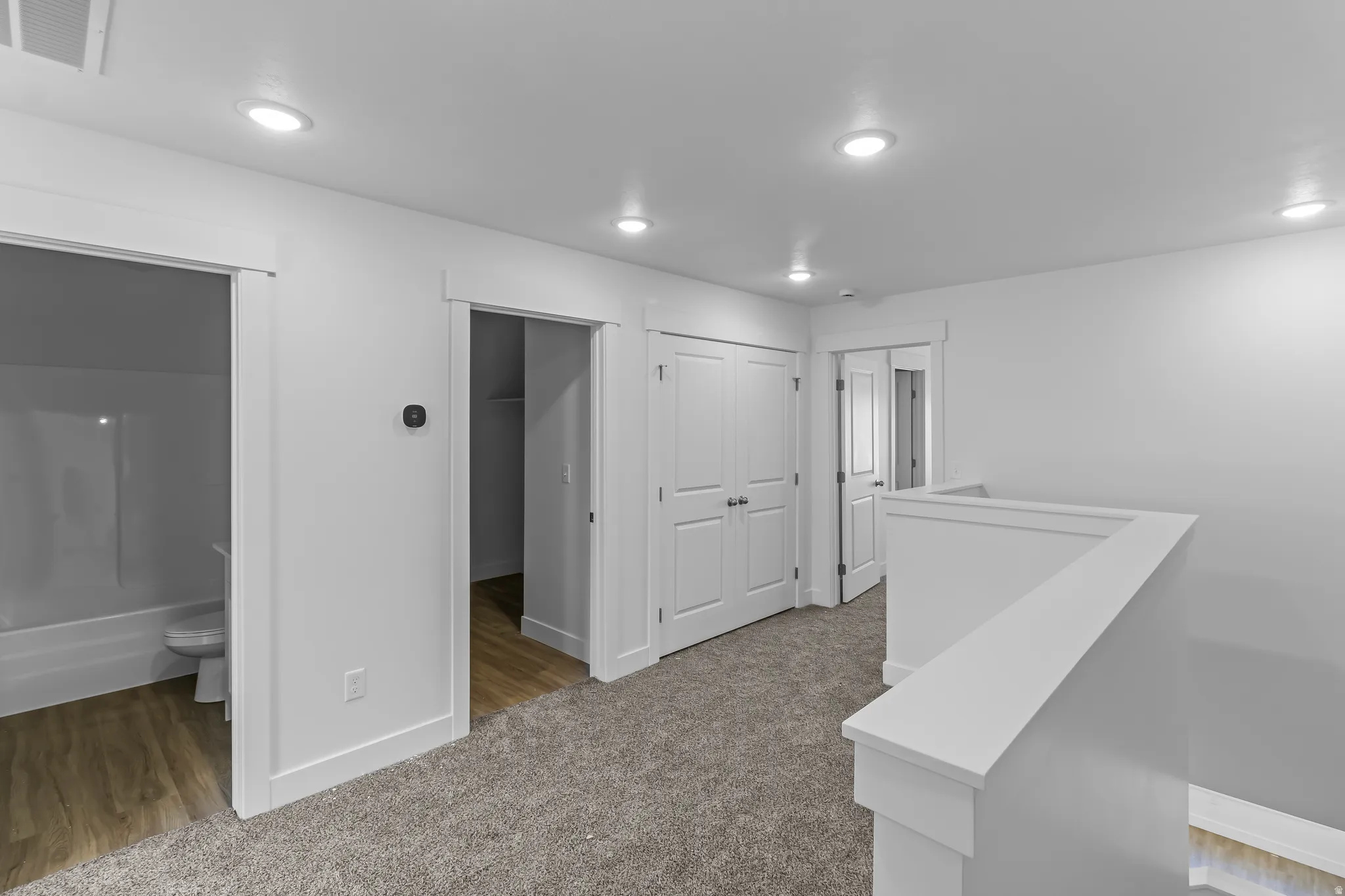 Upper-level landing featuring recessed lighting, gray carpeting, white trim, and a white staircase railing