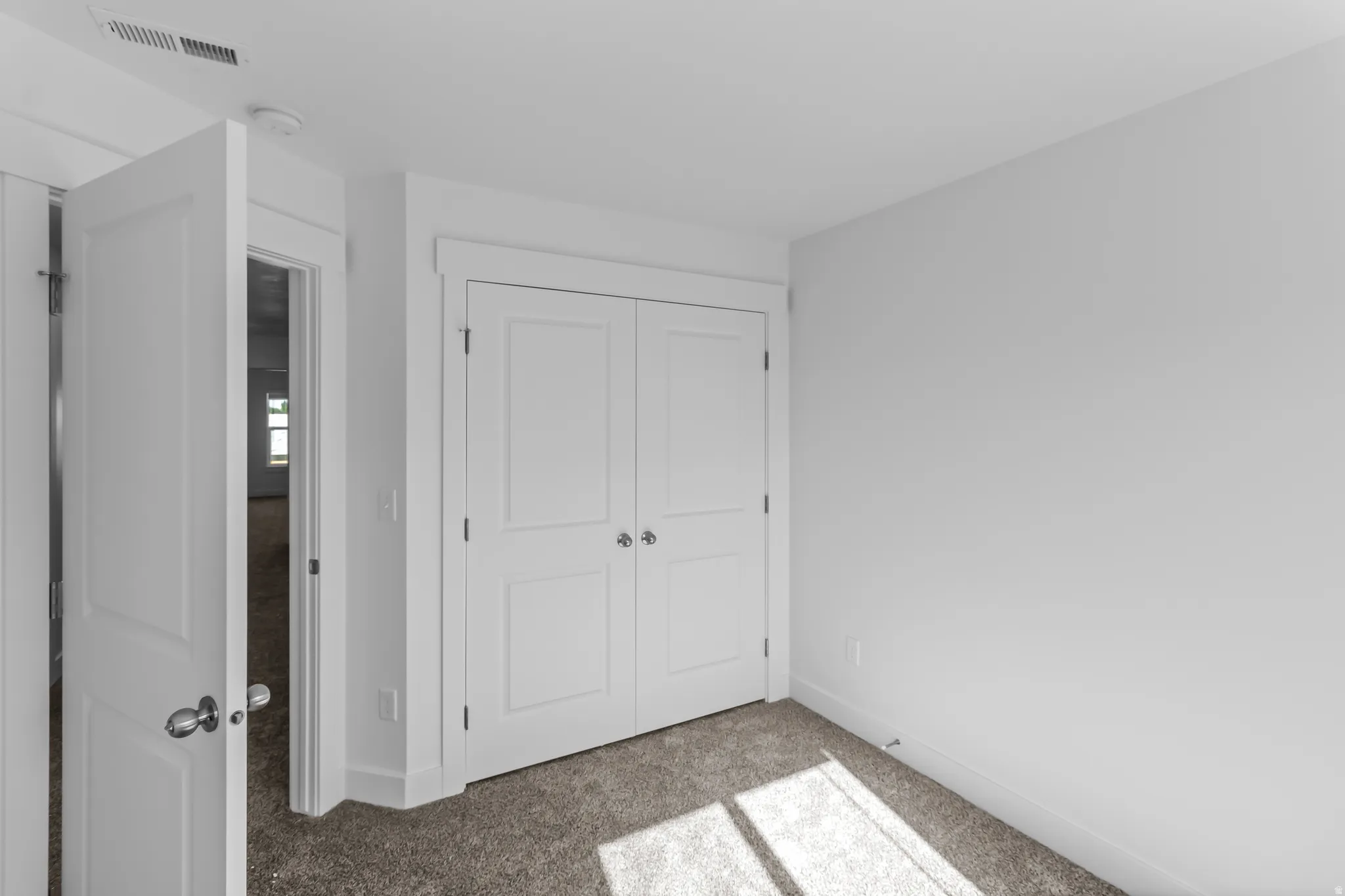 Neutral white wall finishes with matching trim, carpeted flooring, and a double-door closet with polished chrome hardware