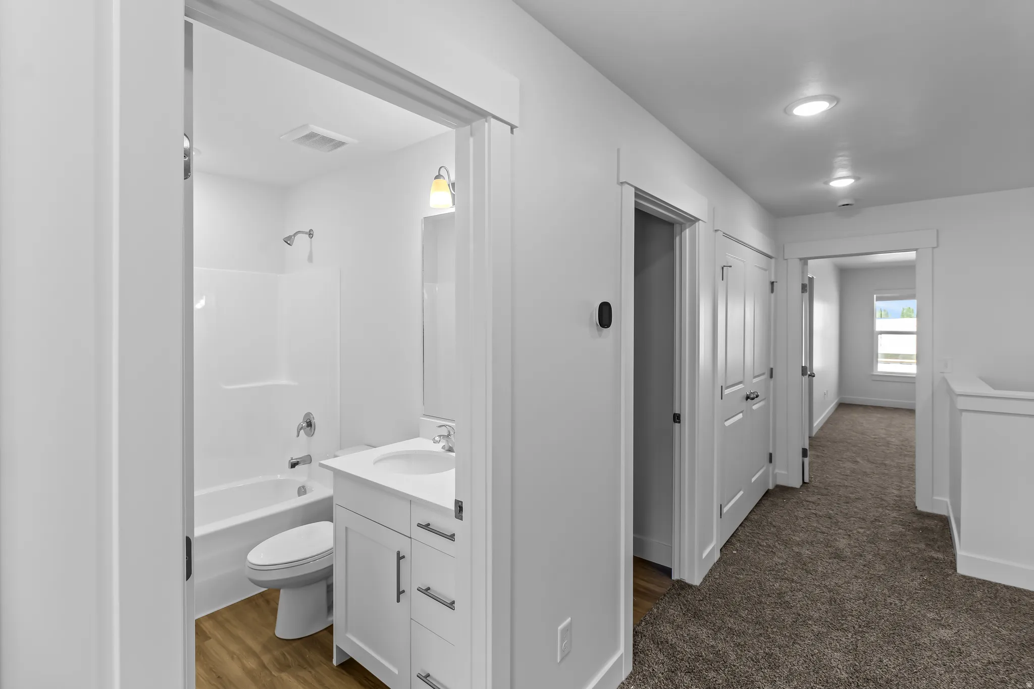Full bathroom with white tub/shower combination, white vanity, and wood-finish flooring
