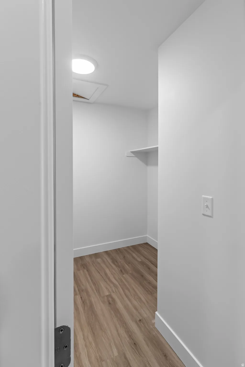 Interior storage space featuring wood-finish flooring, white walls, and a recessed ceiling light