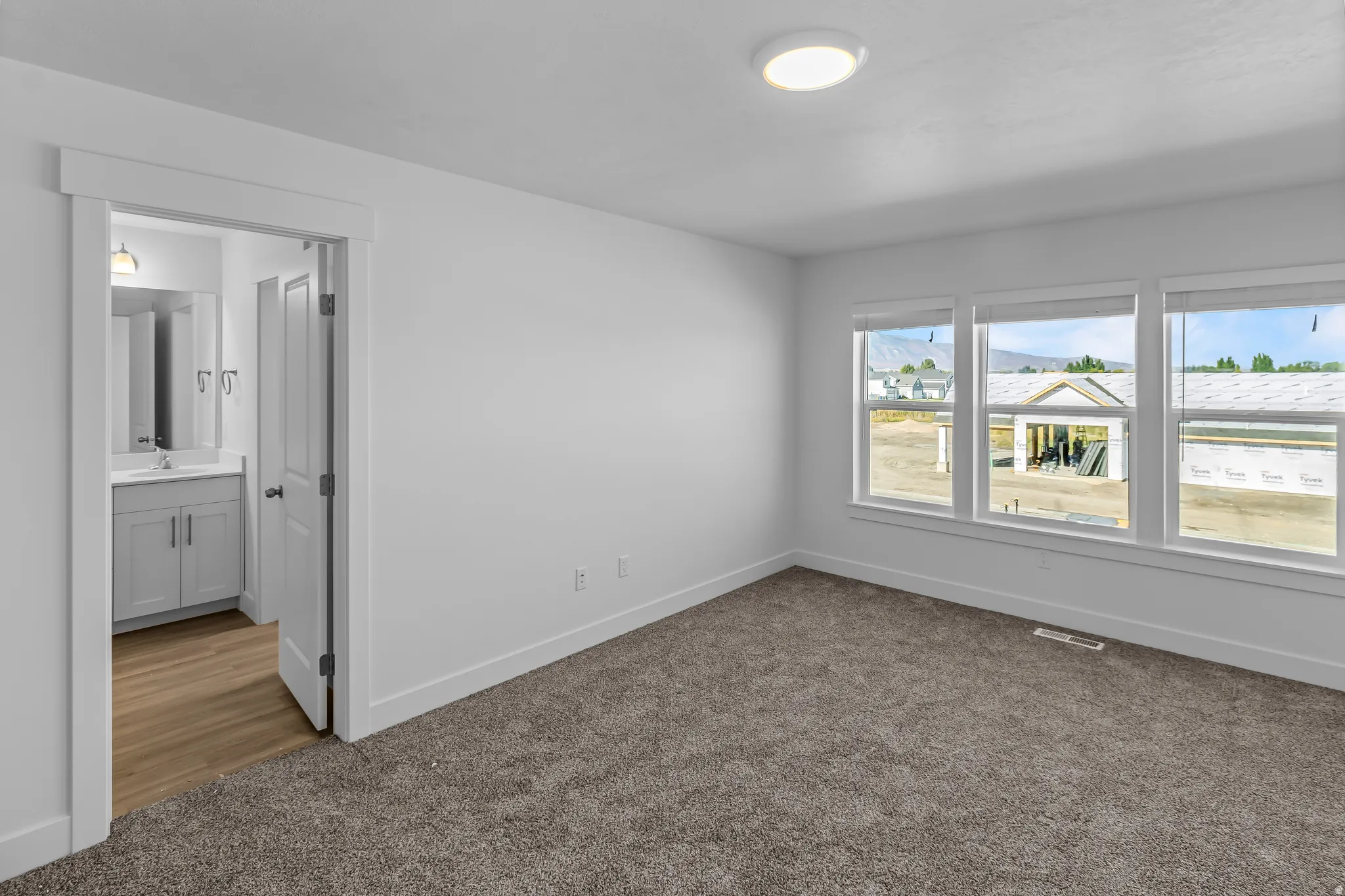 Spacious room featuring three large windows, plush gray carpet, and white baseboards