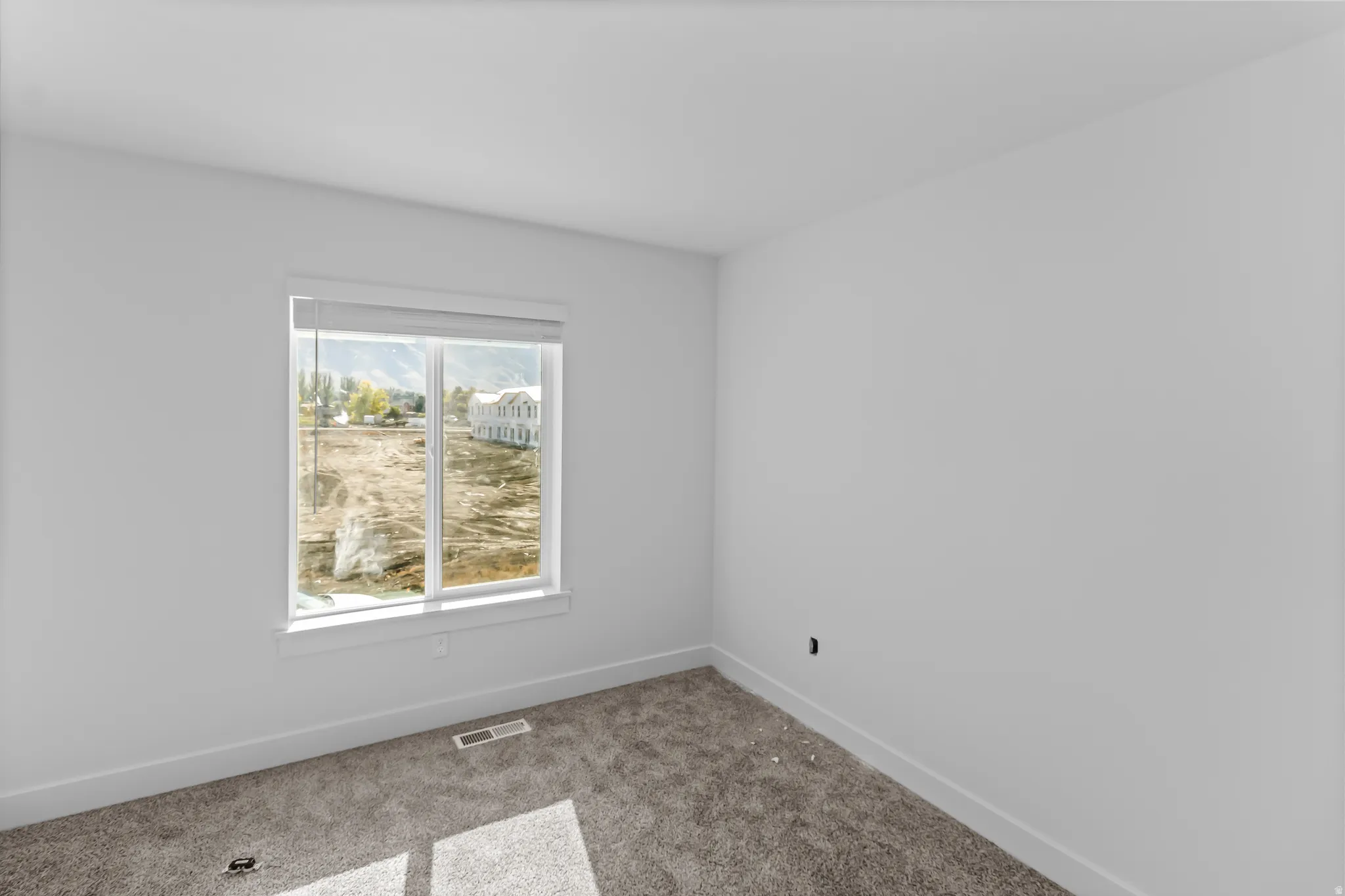Neutral tone walls featuring a large window with white casing, textured grey carpeting, and white baseboards