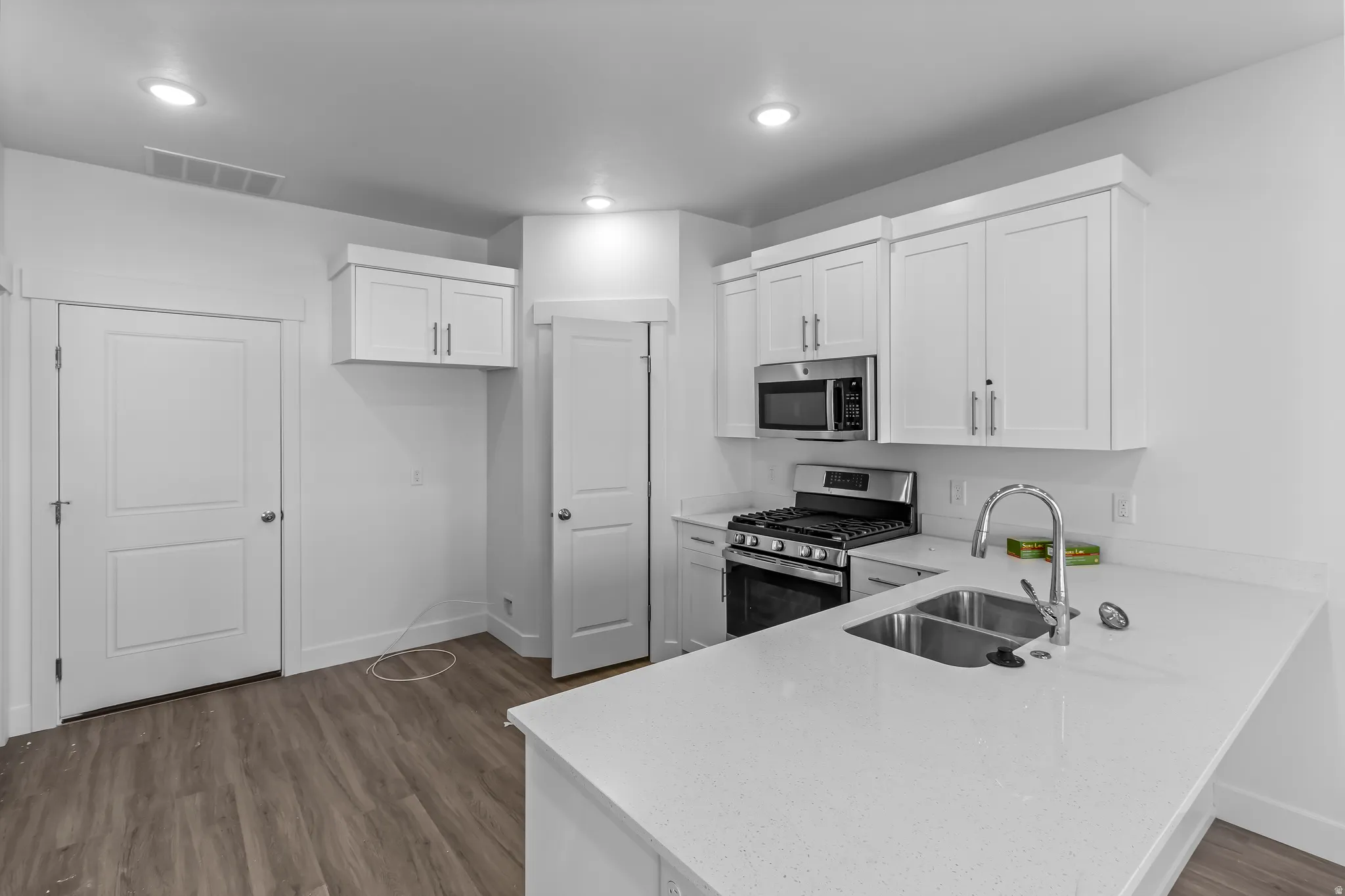 Kitchen featuring white shaker-style cabinetry, a stainless steel gas range with overhead microwave, and a double basin sink with a gooseneck faucet