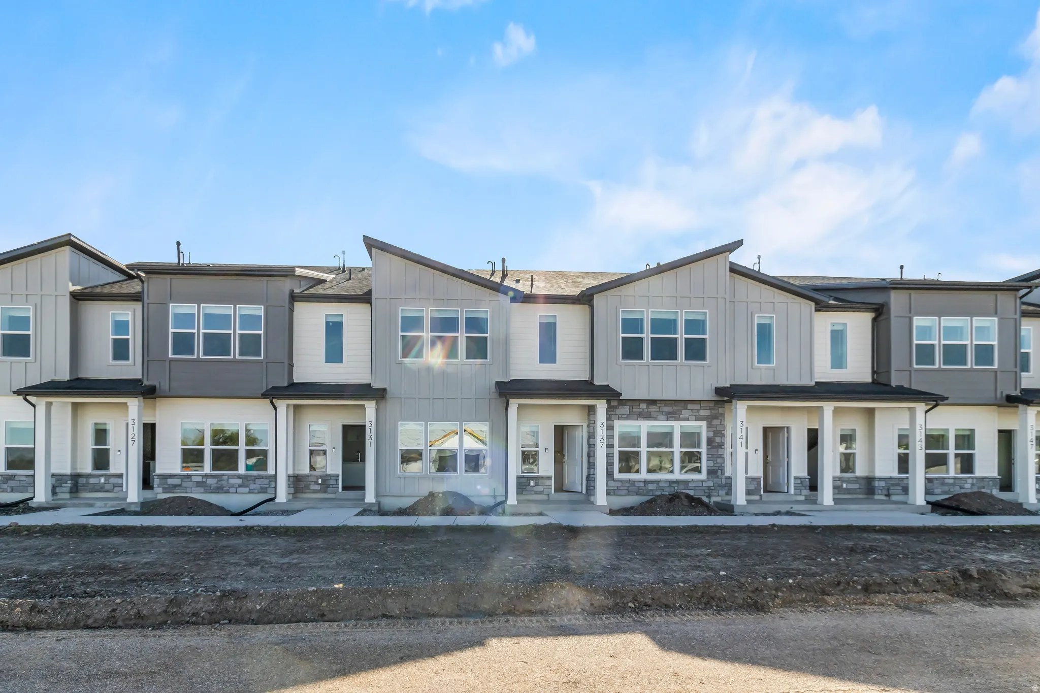 Modern townhome exteriors featuring varied siding textures, stone accents, multiple large windows, covered entryways, and contemporary rooflines