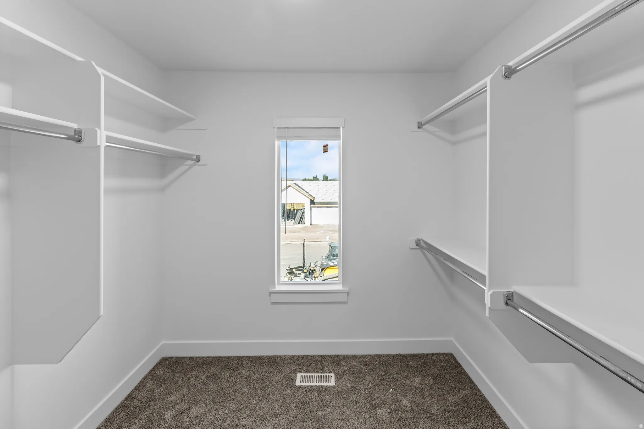Walk-in closet featuring white built-in shelving, chrome hanging rods, and a single window with blinds