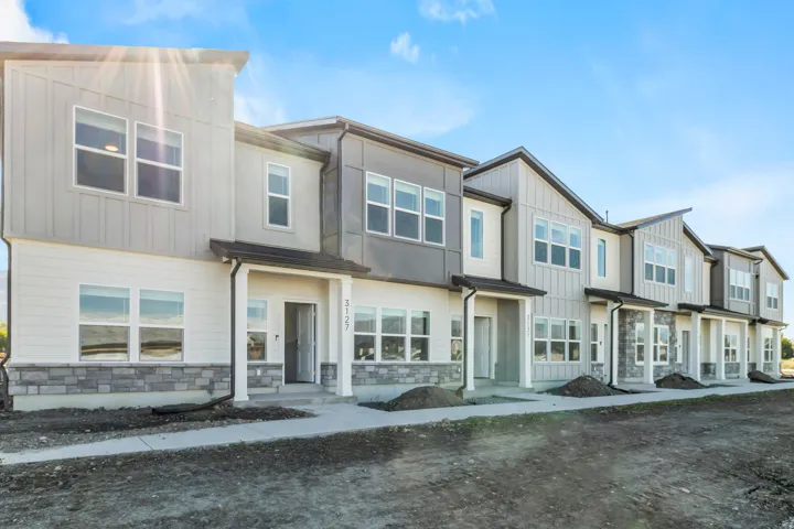 Modern townhome exterior featuring multi-level construction, stone veneer accents, vertical and horizontal siding, multiple windows, and a covered entryway