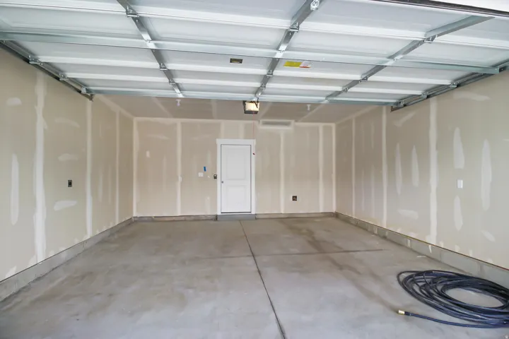 Two-car garage featuring exposed ceiling joists, concrete flooring, and a white interior access door