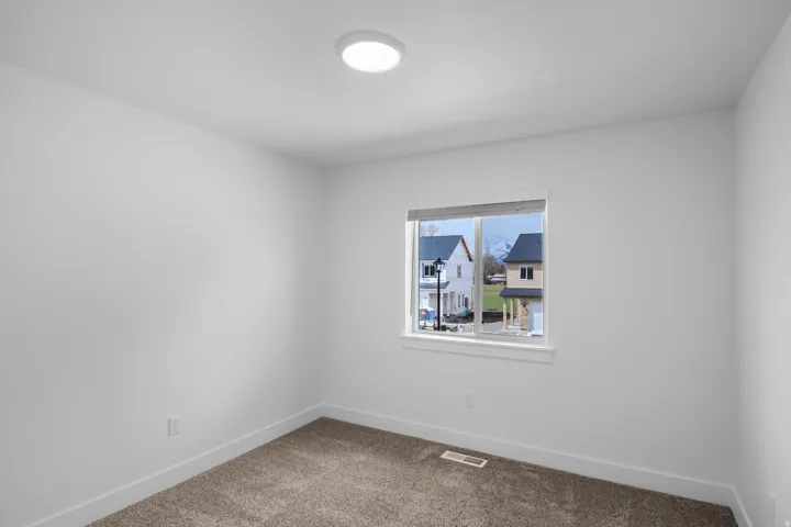 Neutral-toned carpeting complements the white walls and trim in this room featuring a single window and a flush-mount ceiling light