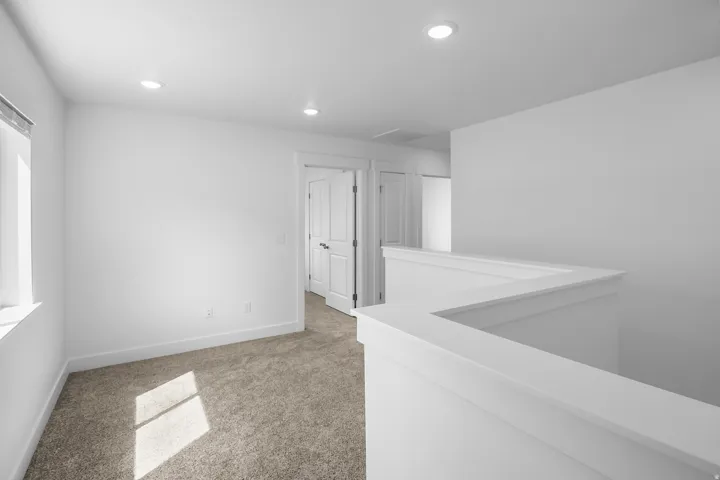 Carpeted upper-level landing with recessed lighting, white walls, and a contemporary railing design