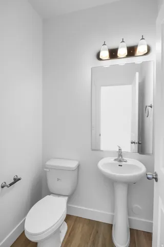 Bright powder room with a pedestal sink, white toilet, and wood-finish flooring
