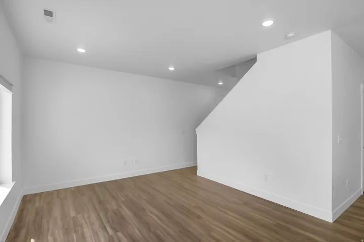 Spacious room featuring wood-finish flooring, recessed lighting, and bright white walls