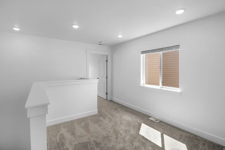 Carpeted loft area featuring a window with horizontal blinds, recessed lighting, and white baseboards