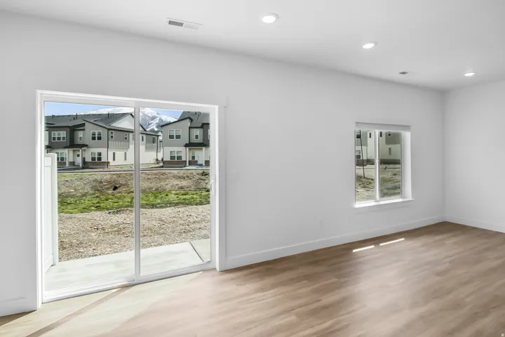 Spacious room featuring light wood-finish flooring, recessed lighting, and a sliding glass door opening to a concrete patio