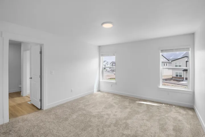 Spacious room featuring neutral carpeting, white walls, two windows with white trim, and a flush-mount ceiling light