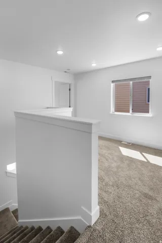 Upper level landing with plush carpet, white painted walls, recessed lighting, and a contemporary window with a dark roller shade