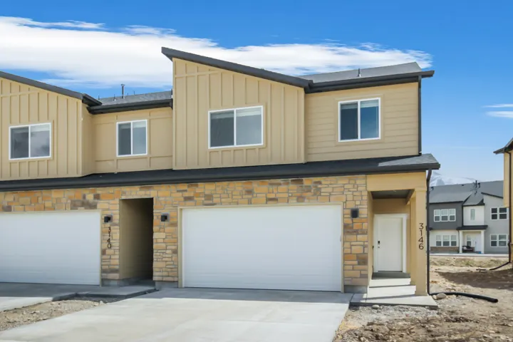 Contemporary townhome exterior featuring an attached garage, stone veneer siding, tan vertical siding, and a covered entry