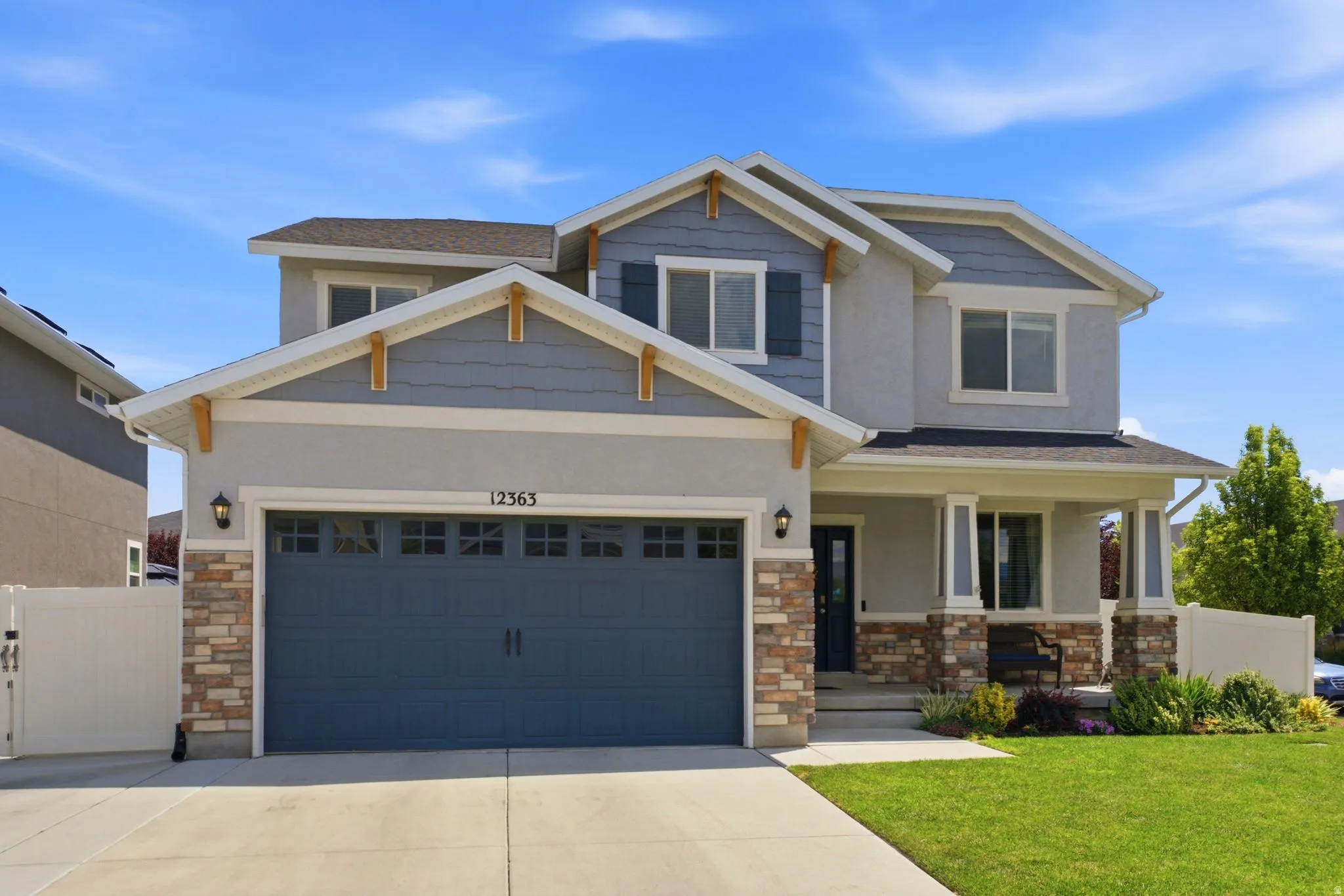 Contemporary residence featuring a two-car garage with a dark blue door, stone accents, and a covered front porch