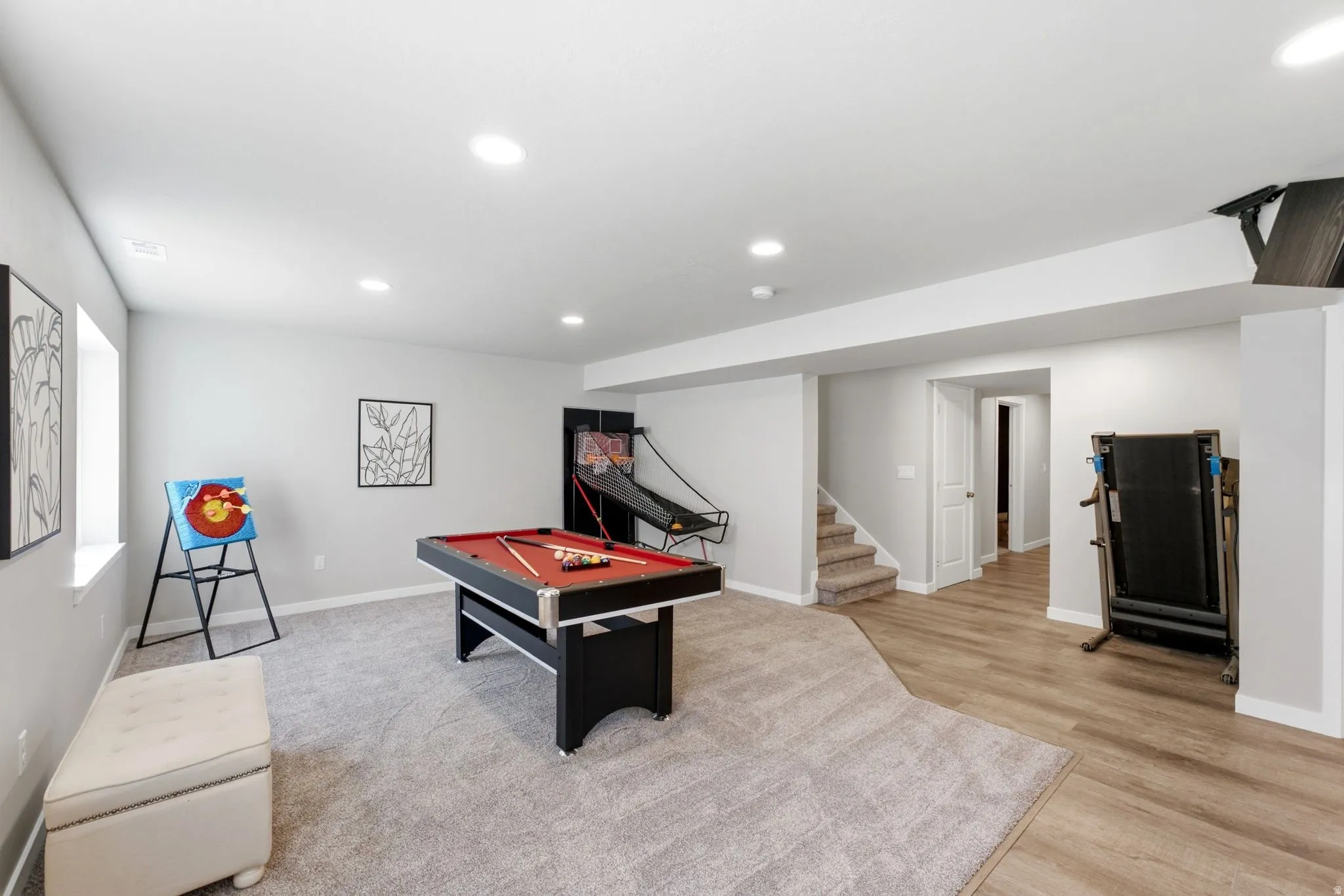 Spacious recreation area featuring a combination of carpet and wood-finish flooring, recessed lighting, and a window for natural light