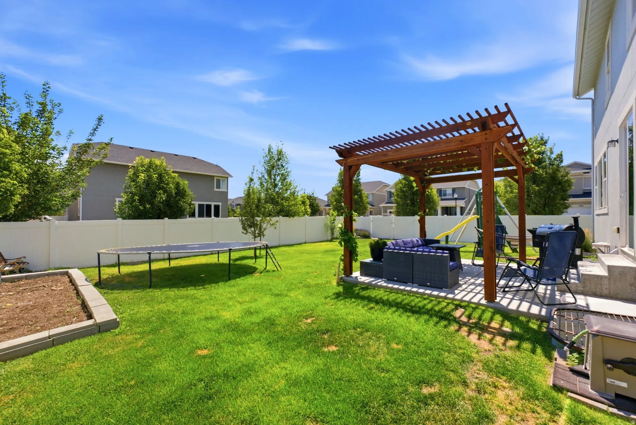 Expansive green lawn with a white vinyl privacy fence and a dedicated garden bed area