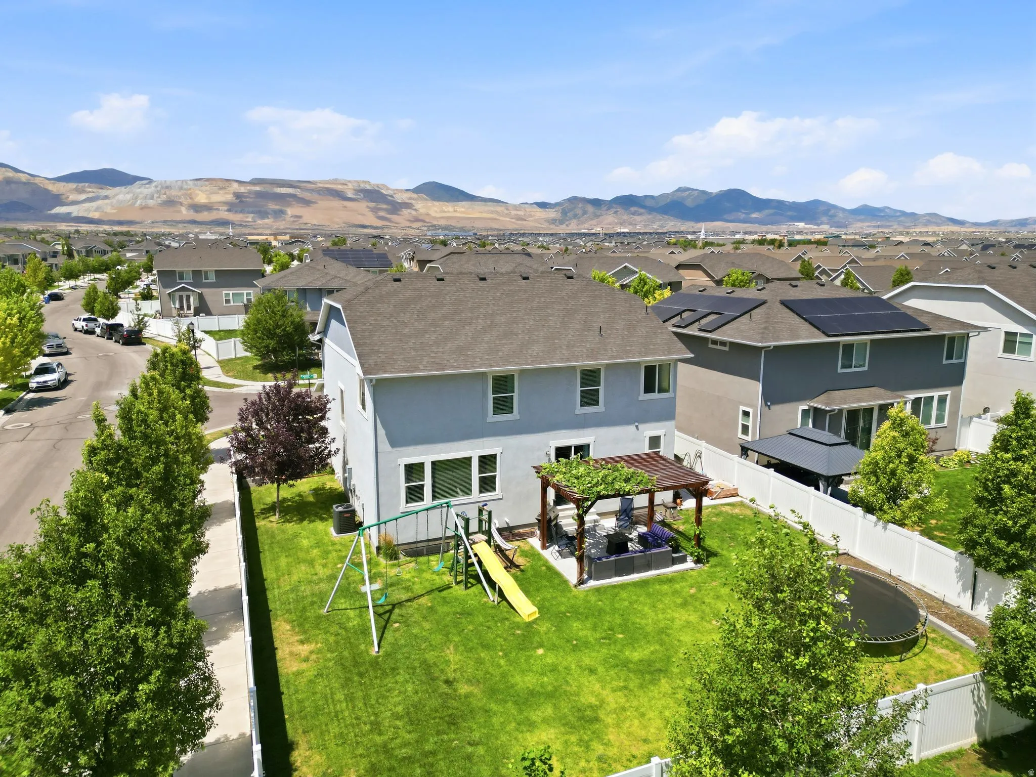 Expansive backyard featuring a lush lawn, a dedicated patio with a pergola, and a white privacy fence