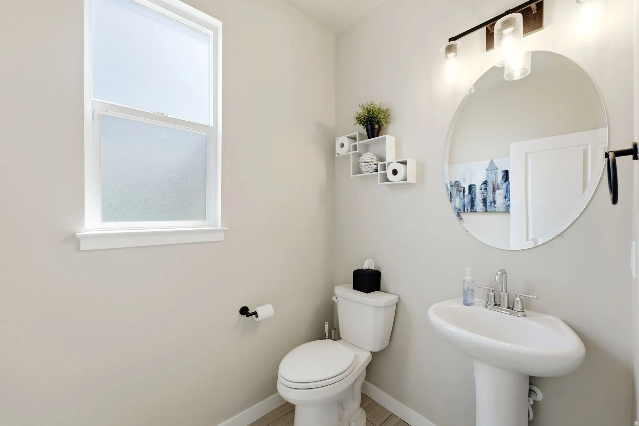 Modern bathroom featuring a white pedestal sink, a circular wall-mounted mirror, and contemporary light fixtures