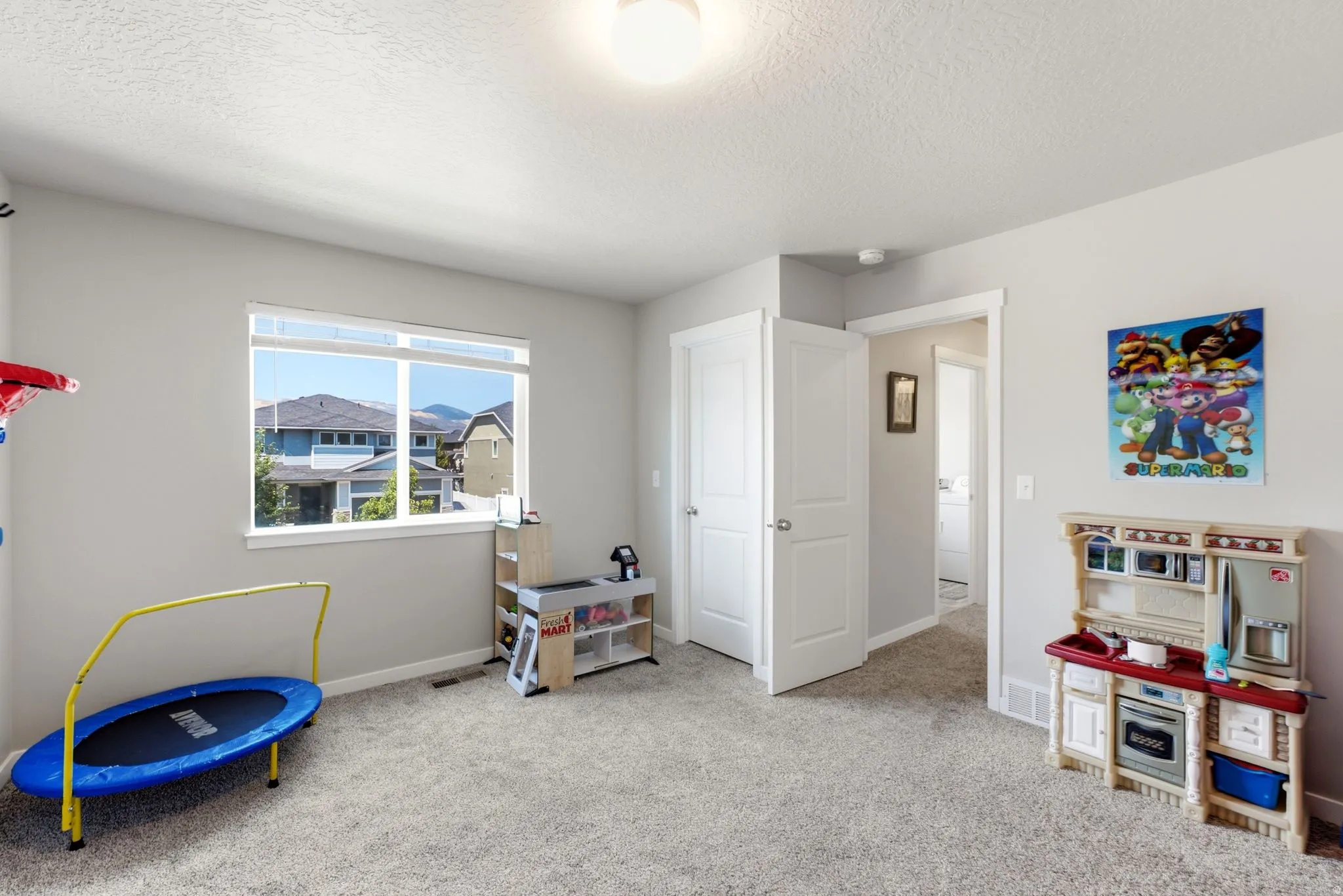 Spacious room featuring light gray walls, plush carpeting, a large window, white trim, and a white interior door with a silver handle