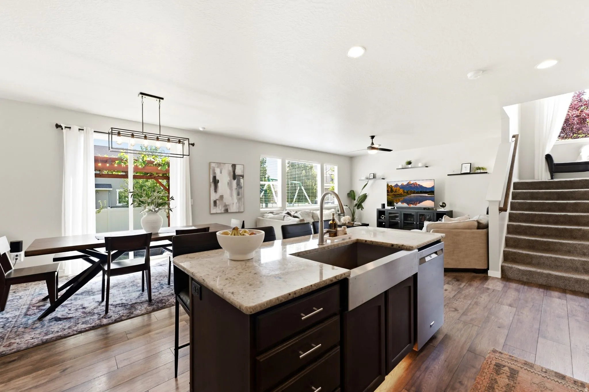 Open-concept living area featuring wood-finish flooring, recessed lighting, and a kitchen island with granite-style countertops and a farmhouse sink