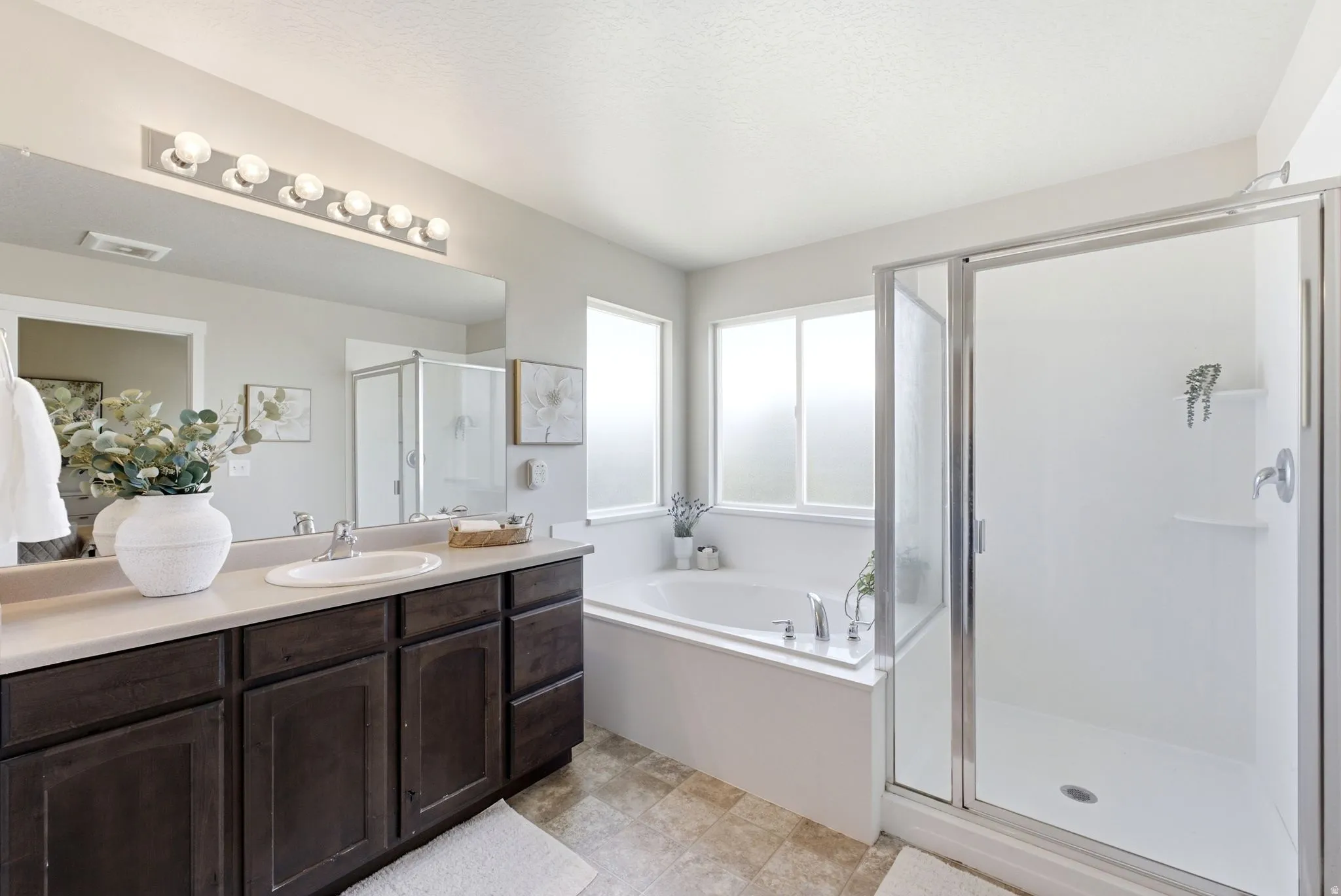 Bathroom featuring a dark wood-finish vanity with an integrated sink, a large mirror, a separate shower with a glass enclosure, and a built-in tub with privacy windows