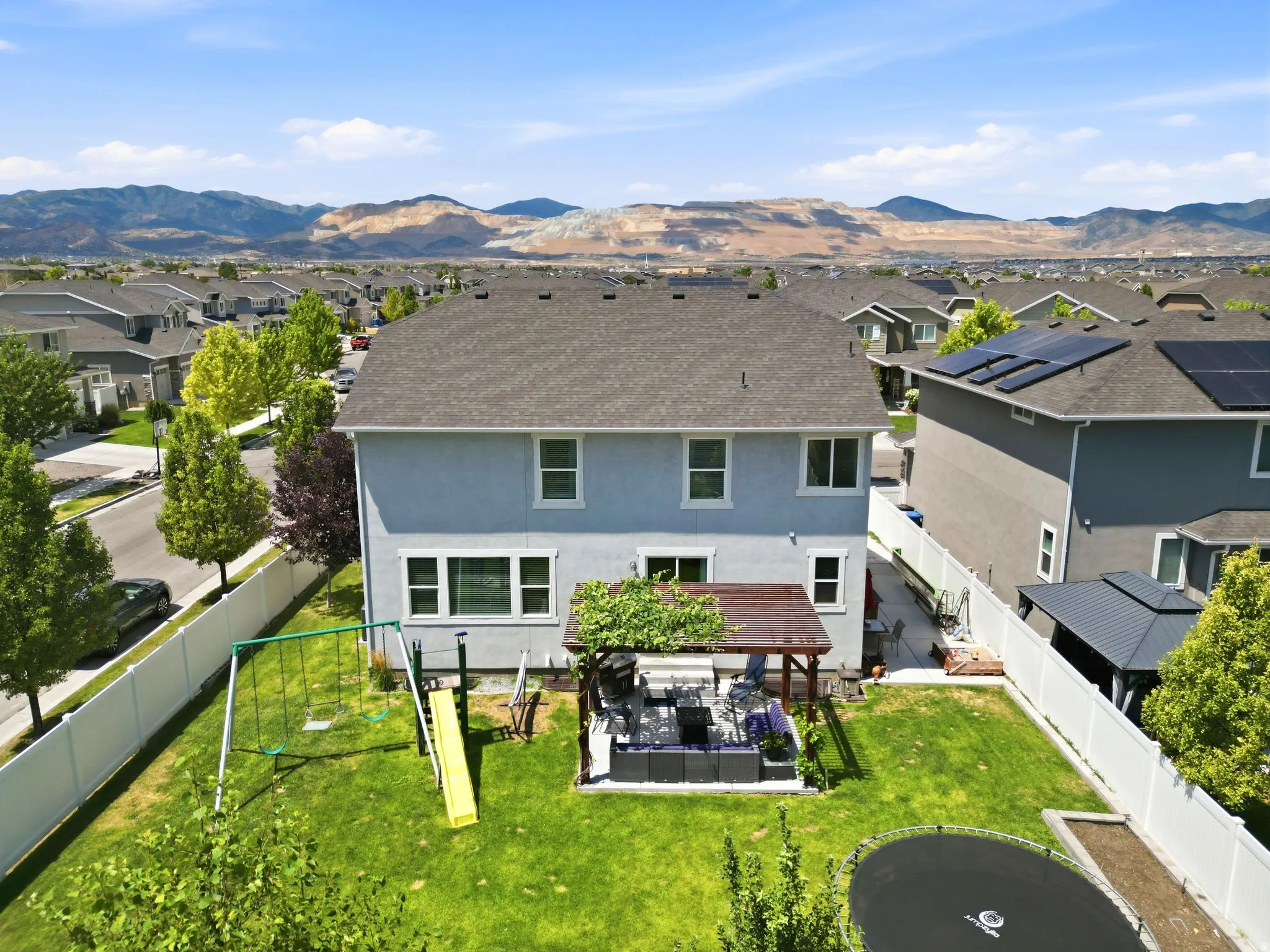 Expansive backyard featuring a covered patio, manicured lawn, and white privacy fencing