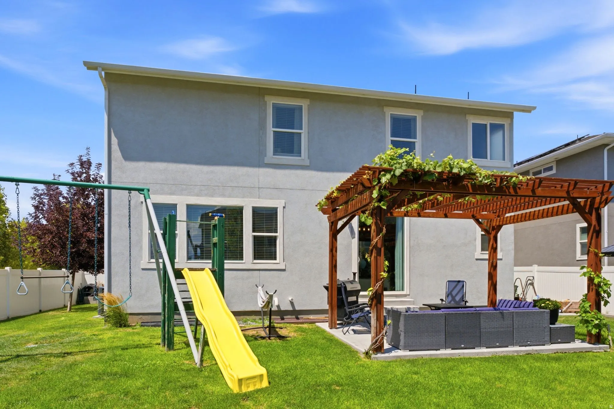 Spacious backyard featuring a large wooden pergola with established vines, a concrete patio, and a manicured lawn
