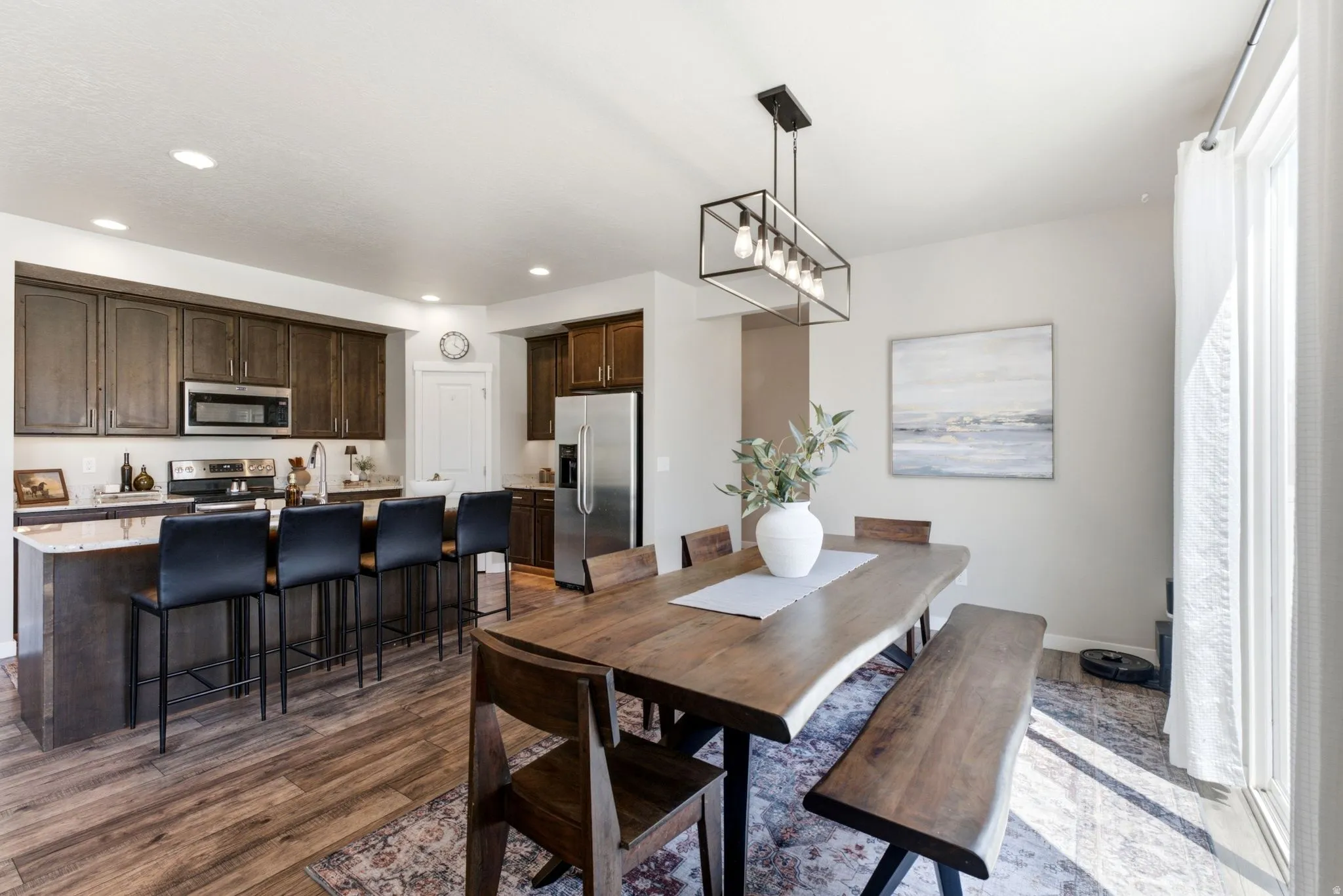 Open-concept kitchen and dining area featuring wood-finish flooring, recessed lighting, and a modern linear chandelier