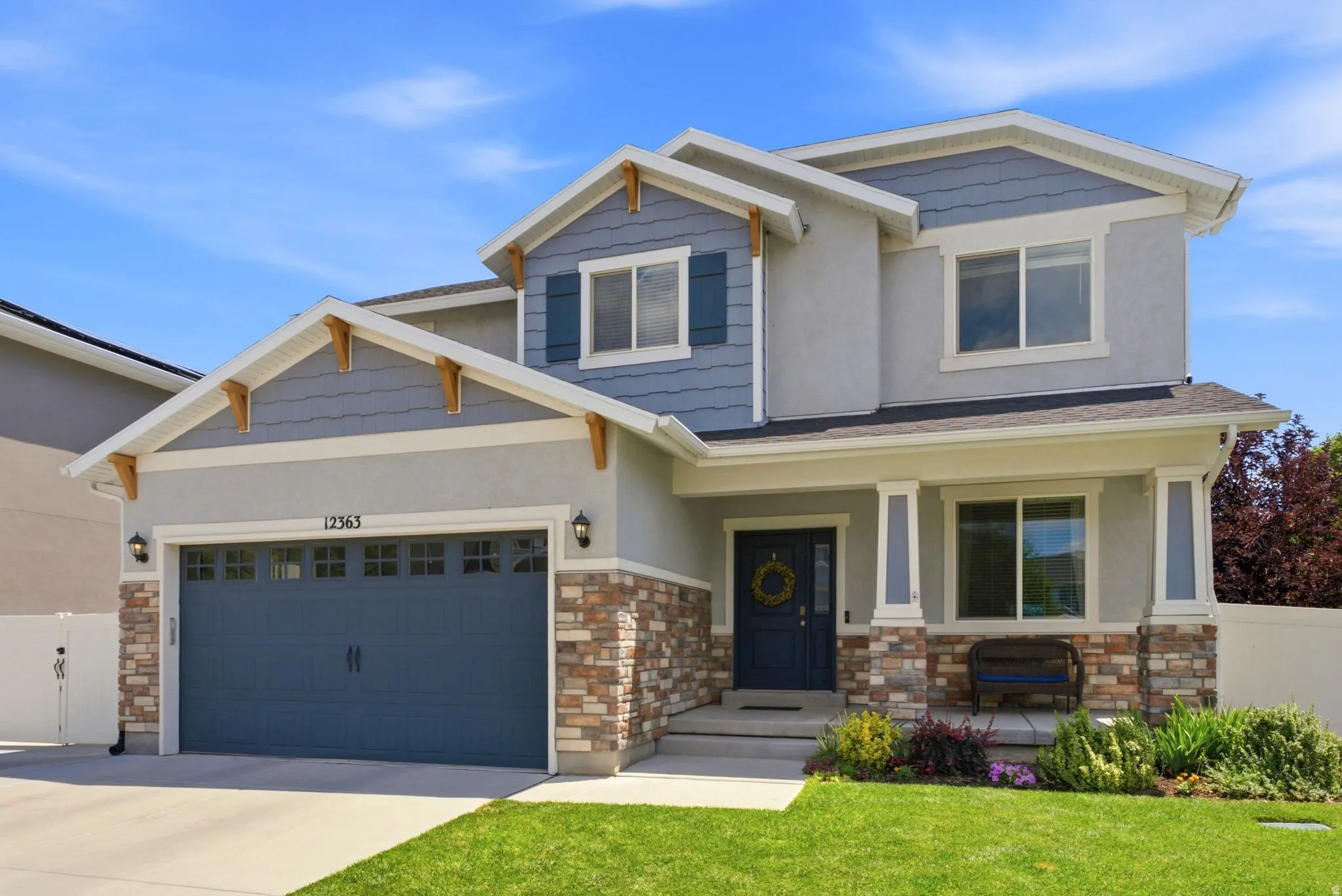 Two-story residence featuring a covered front porch with stone accents, a deep blue main entry door, and a two-car garage with overhead lighting