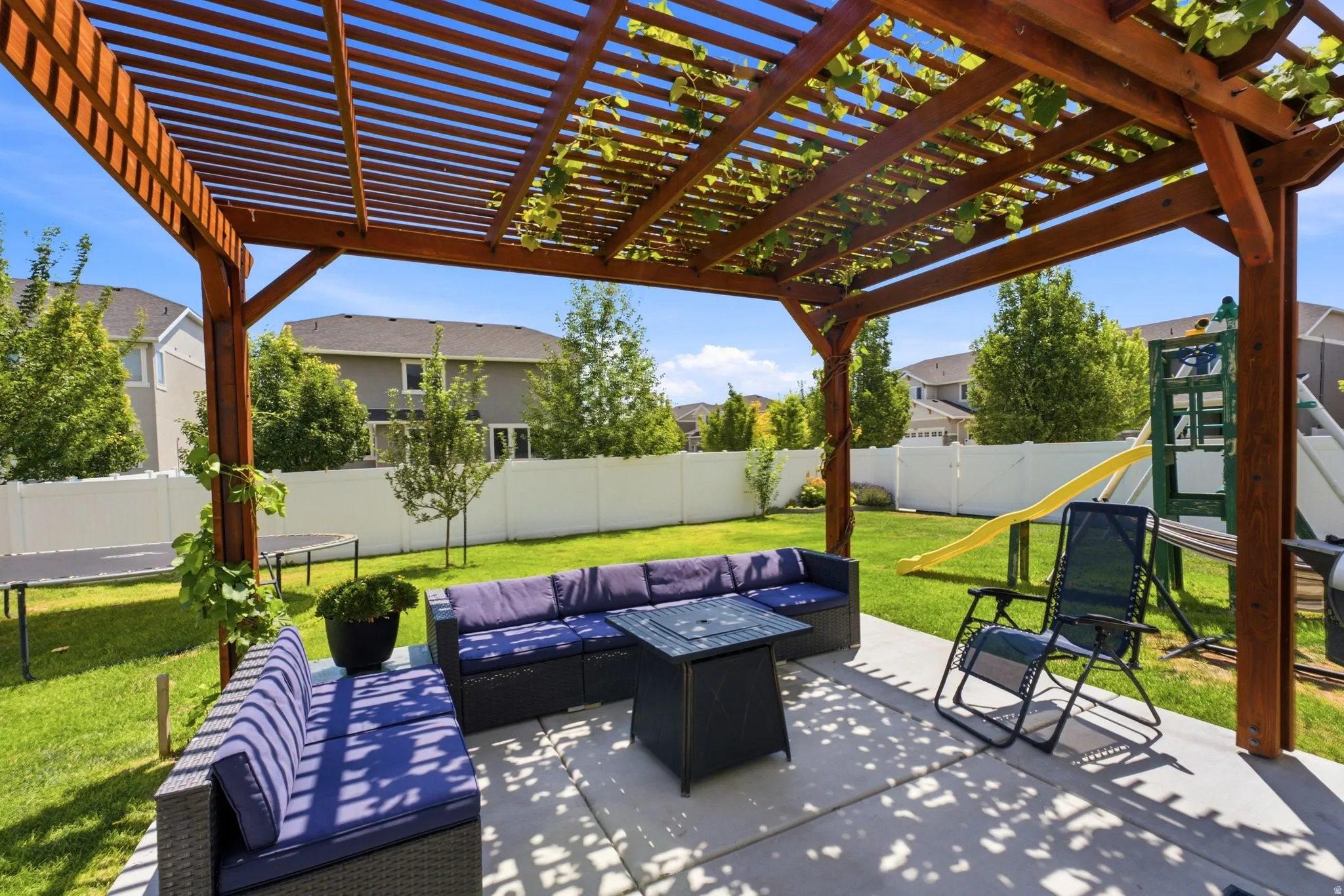 Expansive concrete patio featuring a wooden pergola with vine accents