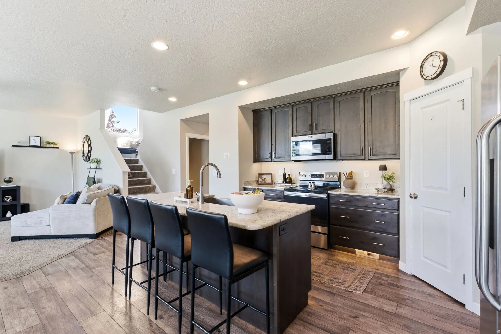 Open-concept kitchen featuring a central island with bar seating, gray cabinetry, stainless steel appliances, light-colored countertops, and wood-finish flooring