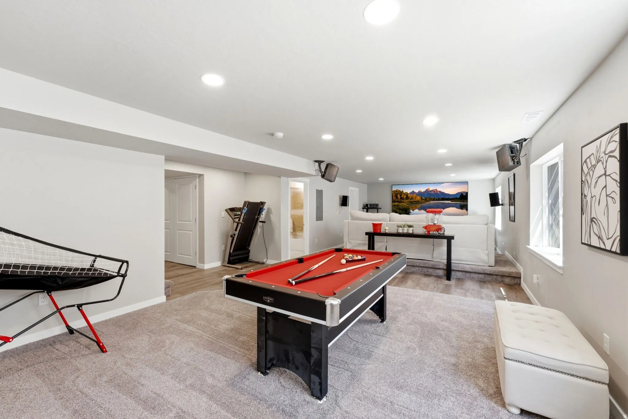 Spacious recreation room featuring recessed lighting, light gray carpeting, and a dedicated media area with a large projection screen