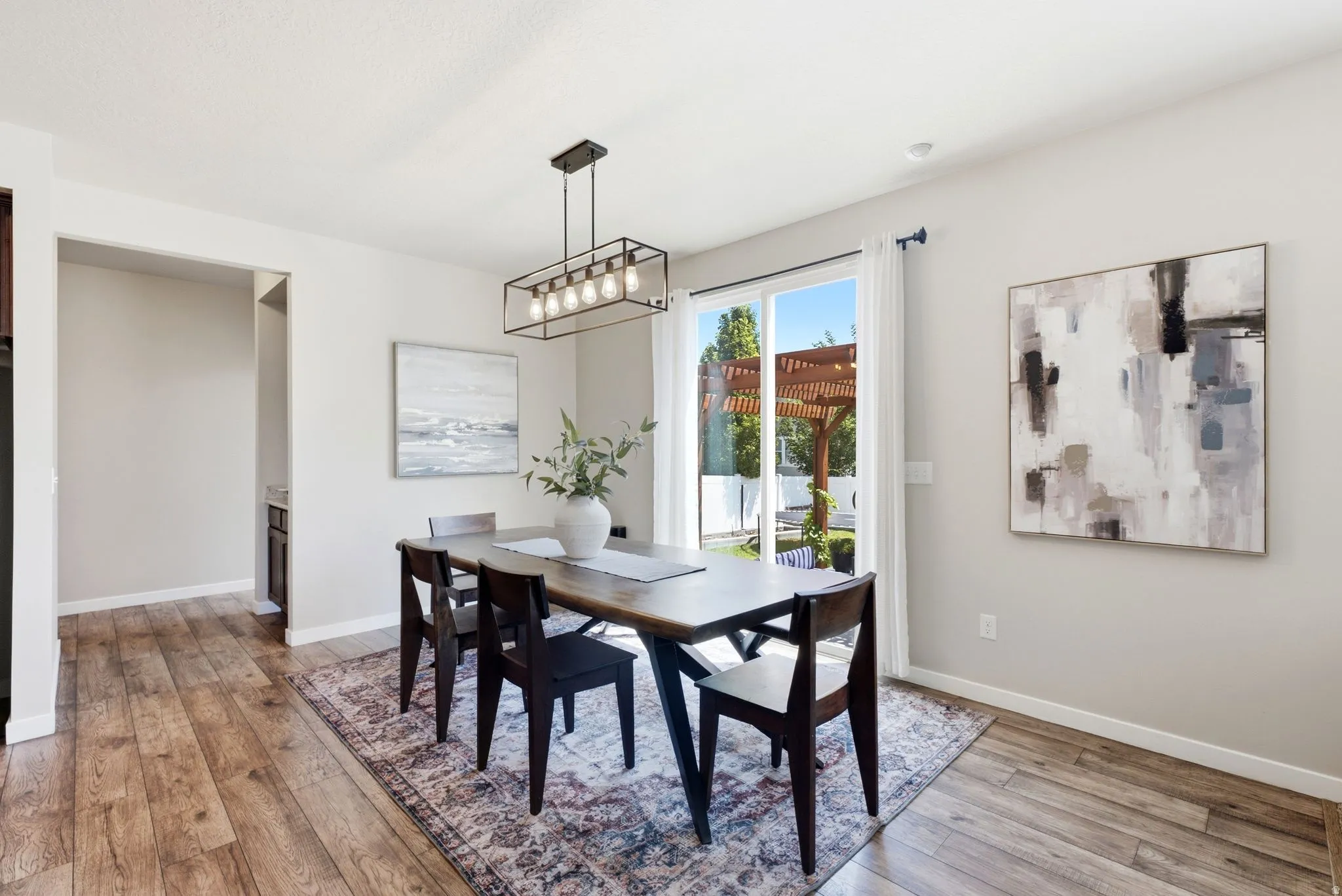 Dining area featuring wood-finish flooring, a modern linear chandelier, and a sliding glass door opening to a pergola-covered patio