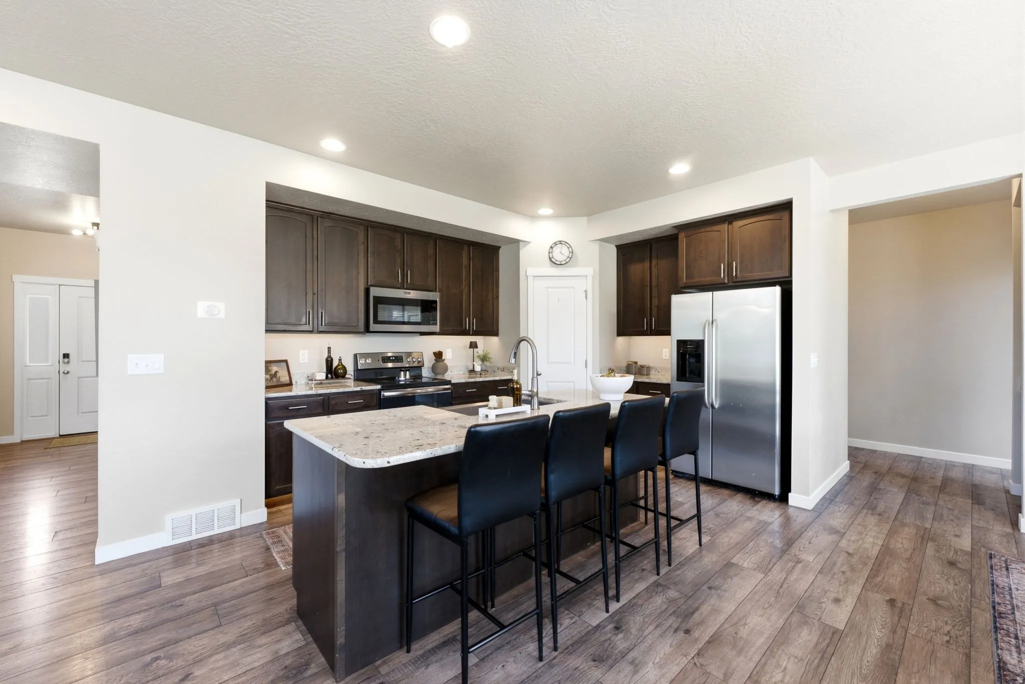 Open-concept kitchen featuring an island with counter seating, dark wood cabinetry, stainless steel appliances, speckled countertops, and wood-finish flooring